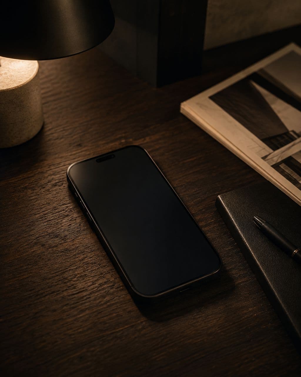 A phone lying face up on a dark desk late at night, its screen dark.